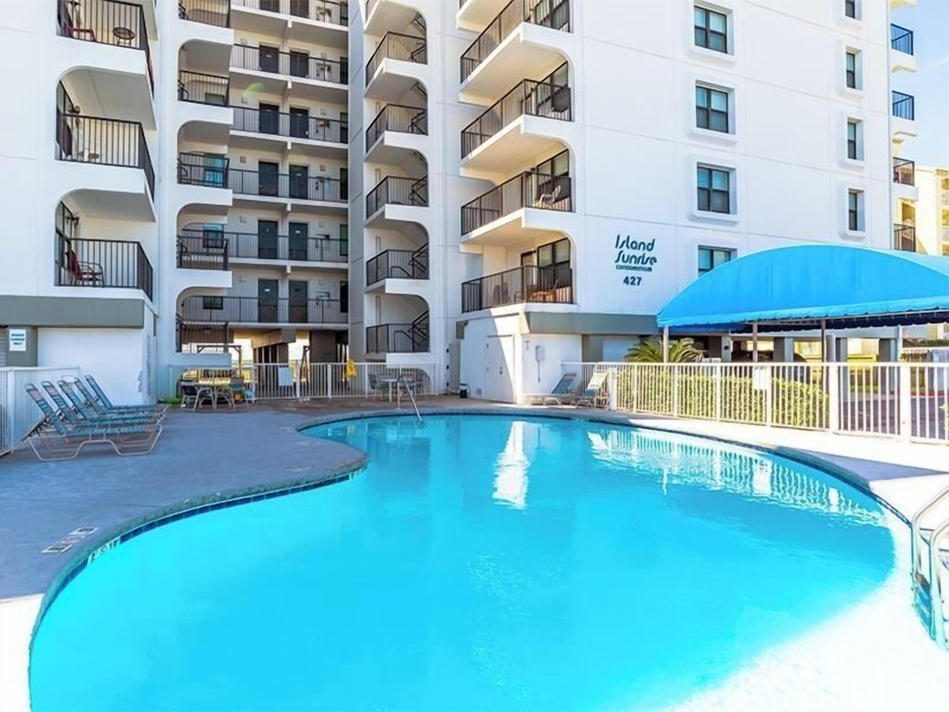 A multi-story hotel with a swimming pool, outdoor seating, and a covered area.