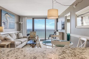Une chambre d’hôtel moderne dotée d’un balcon, d’une grande fenêtre, d’un canapé, d’une table à manger et d’un tableau représentant un oiseau.