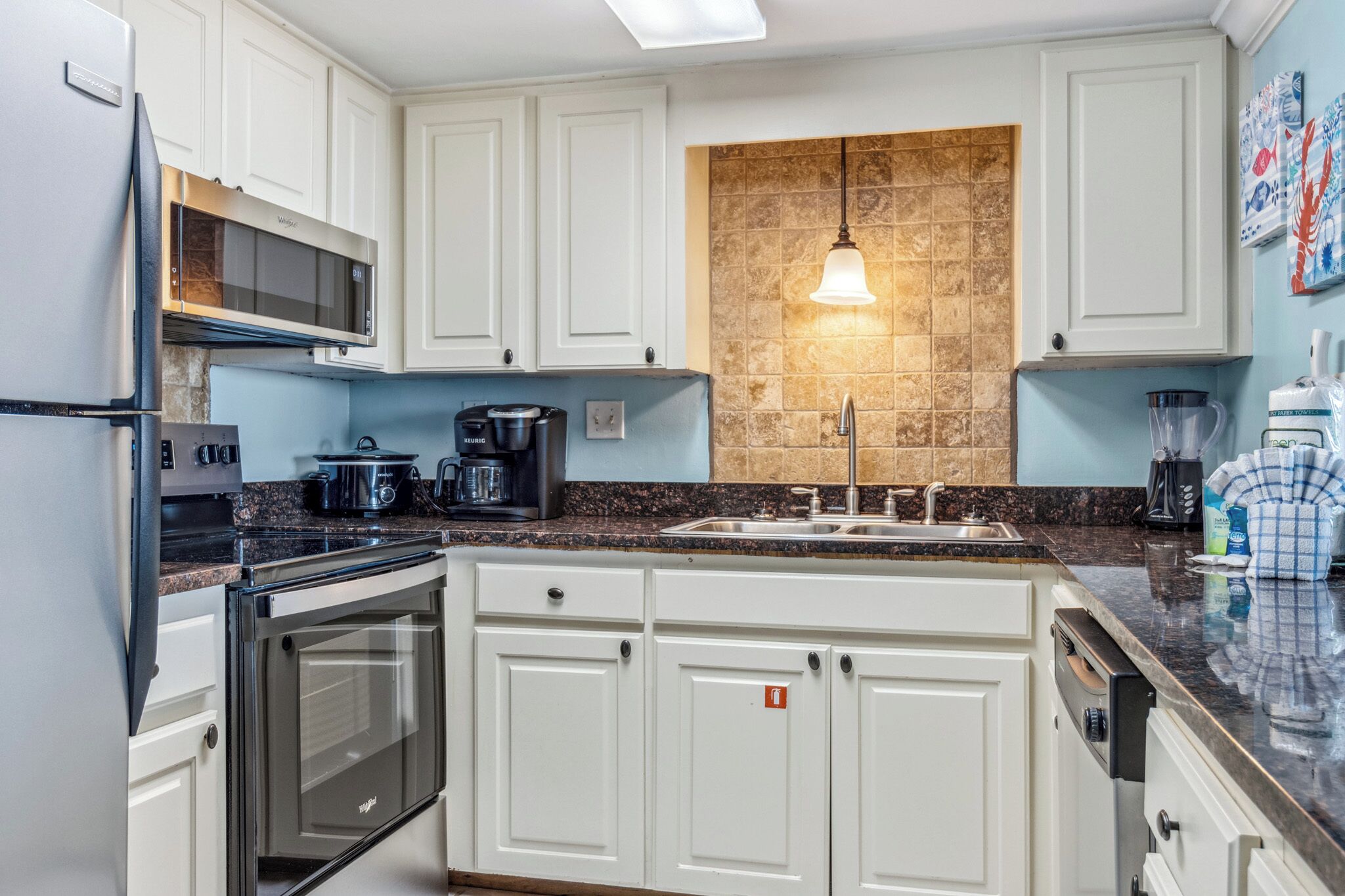 A kitchen with white cabinets, a granite countertop, a built-in oven, a microwave, a coffee maker, and a sink.