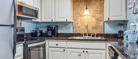 A kitchen with white cabinets, a granite countertop, a built-in oven, a microwave, a coffee maker, and a sink.