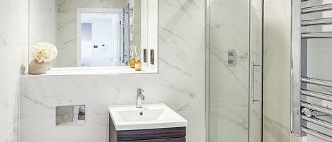 Un baño moderno con ducha envuelta en vidrio, un lavamanos blanco y un mueble de tocador de tonos oscuros.