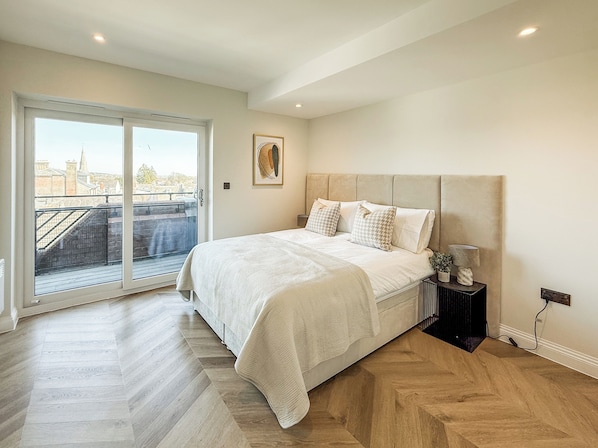 A bedroom with a large bed, a nightstand, a painting, and a view through a sliding door.