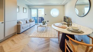 A modern living room with a sofa, a dining table with chairs, a large mirror, and a view through a glass door. - 1 Bed Flat - Sleeps 2 - Parking - Wifi (Dorchester)