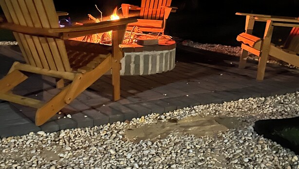 A fire pit with two Adirondack chairs and a table, surrounded by gravel.