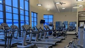 Un gimnasio con múltiples cintas de correr y máquinas de ejercicio, ventanas amplias y luces en el techo.