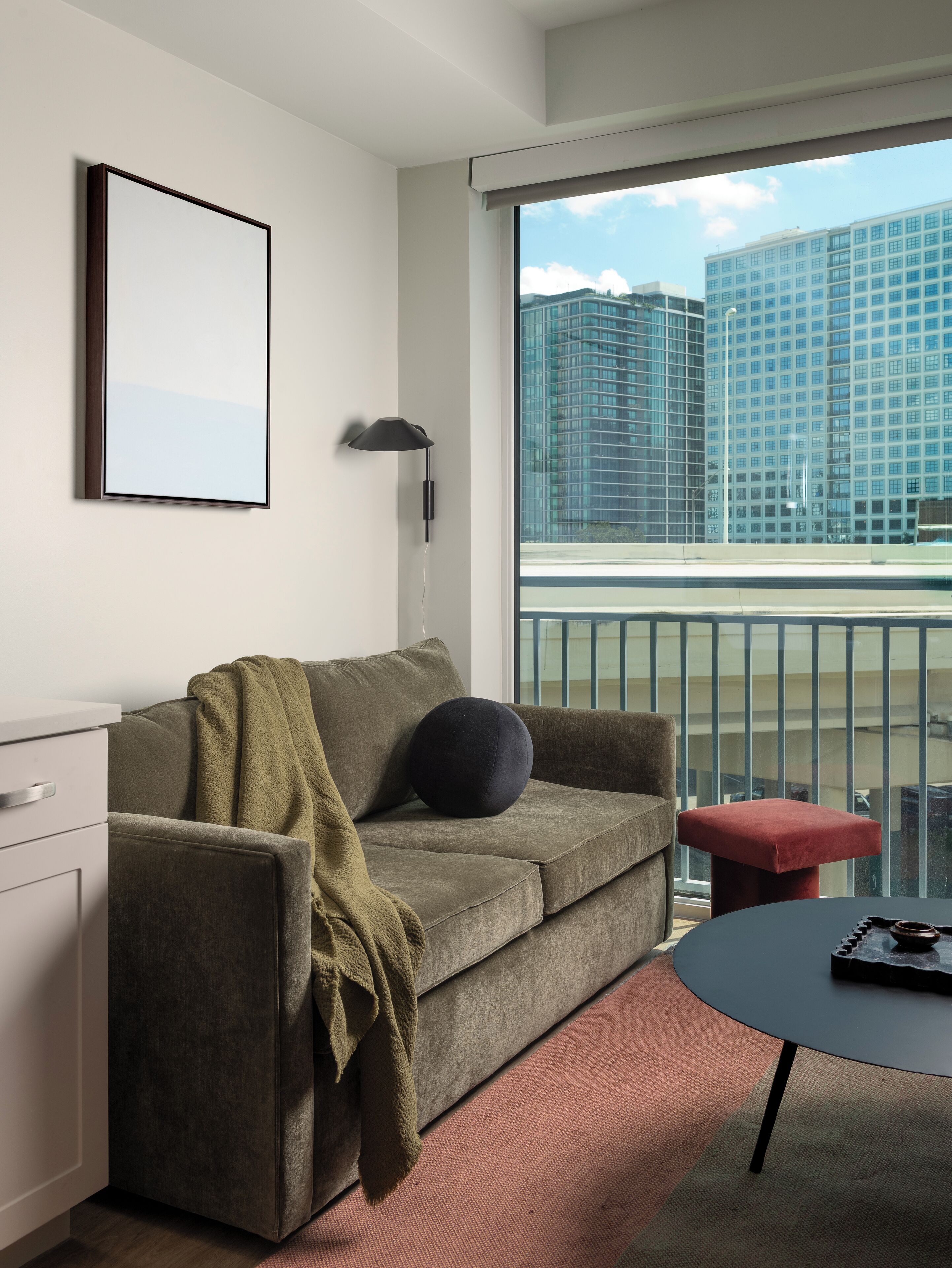Ein modernes Wohnzimmer mit einer Couch, einem kleinen Tisch und Blick auf hohe Gebäude.