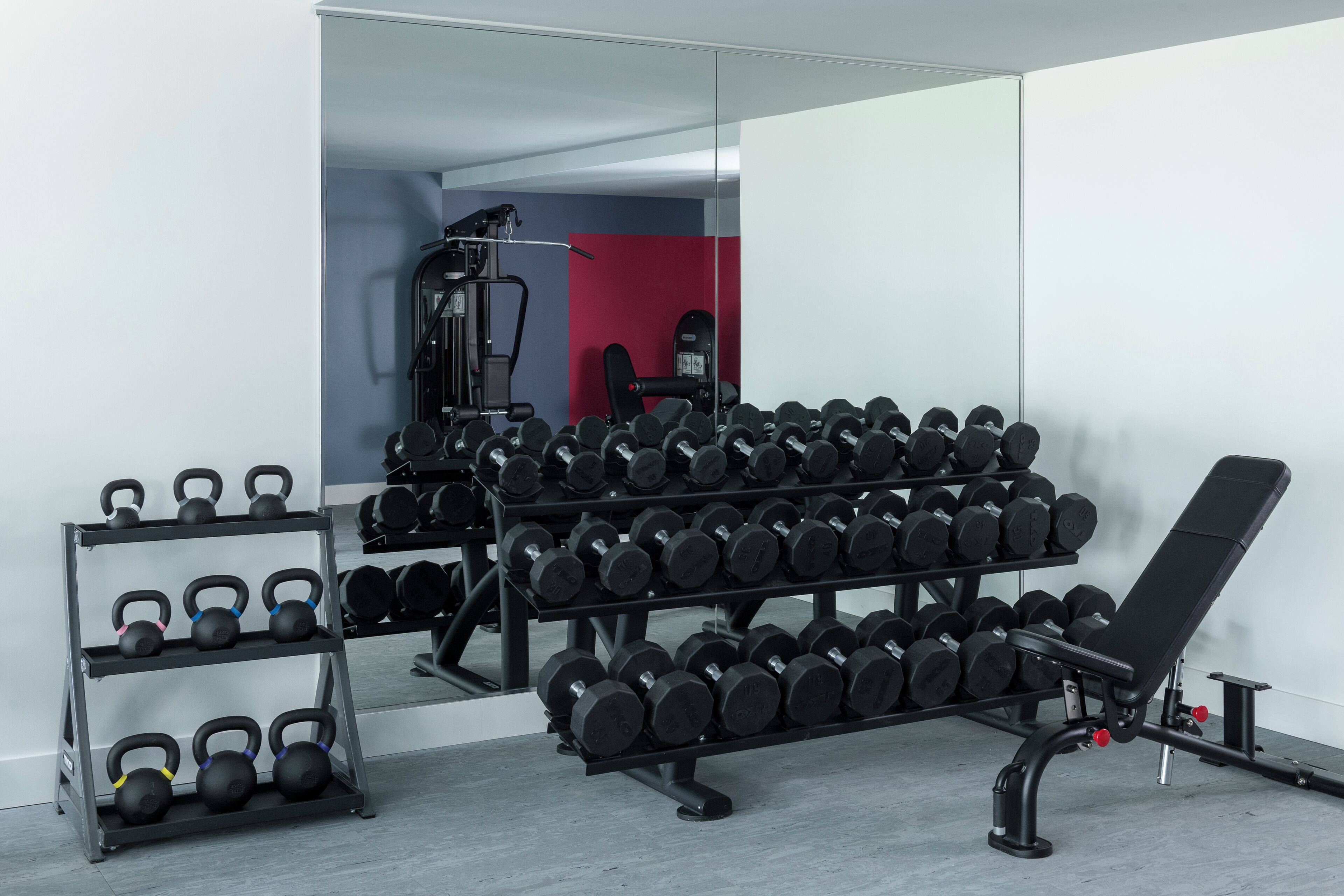 A gym with a bench, kettlebells, and dumbbells.