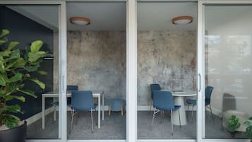 Uma sala de reuniões moderna com paredes de vidro, mesa branca, cadeiras azuis e um vaso de planta.