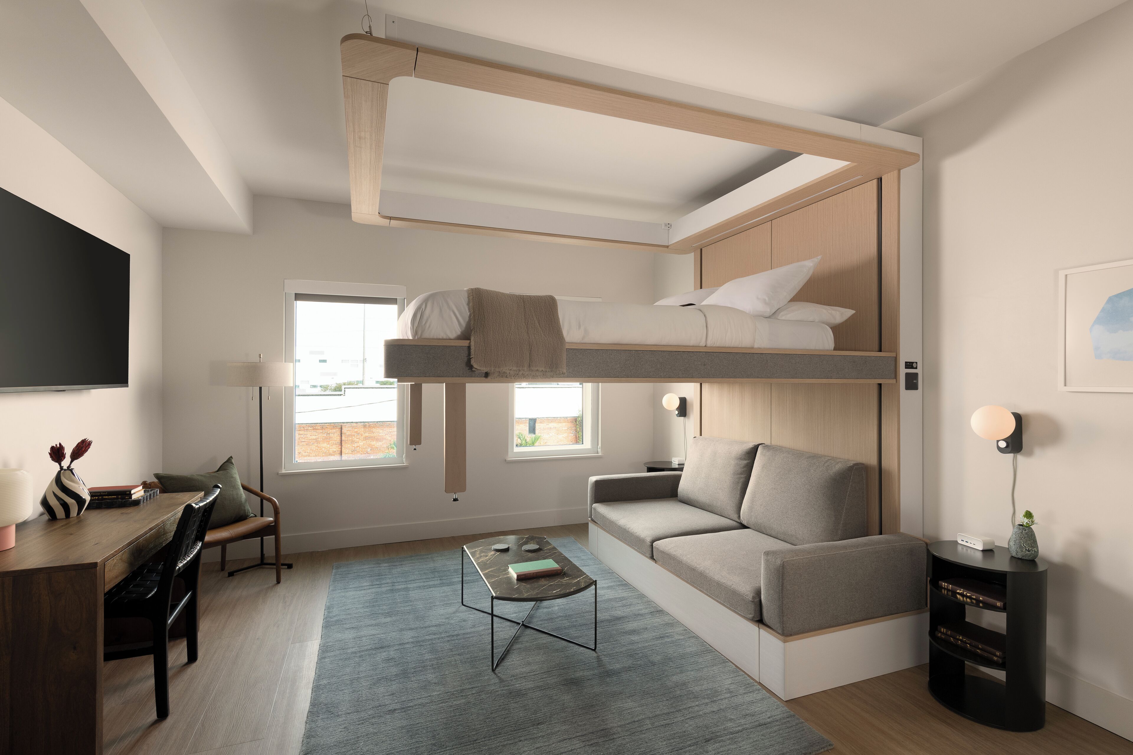 A modern, compact living space with a bunk bed, a sofa, a desk with chairs, and a coffee table.