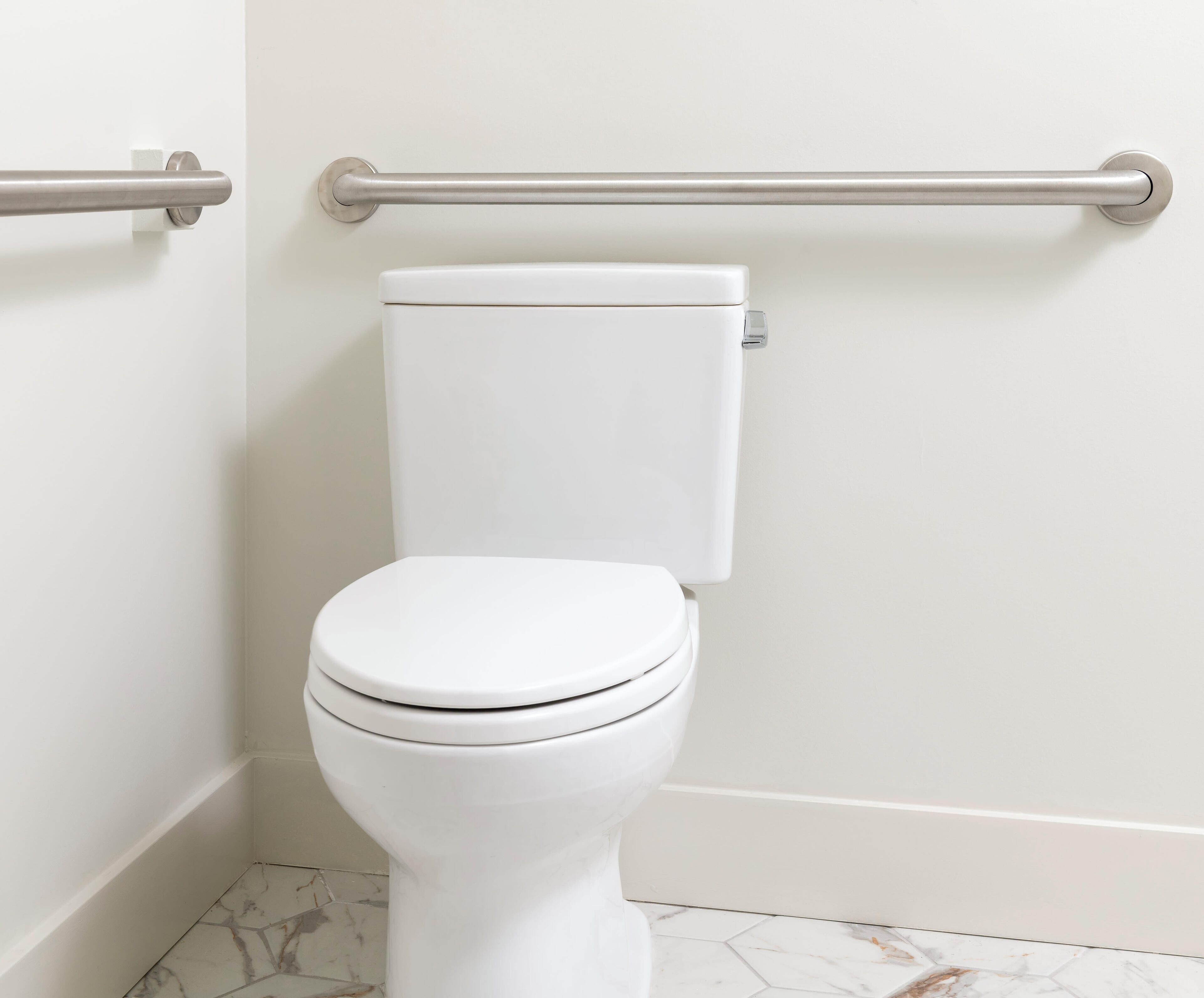 A white toilet with a marble-patterned floor, a metal grab bar, and a white wall.