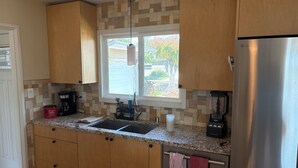 Una cocina con gabinetes de madera, encimera de granito, refrigerador de acero inoxidable, ventana con vistas y cafetera.