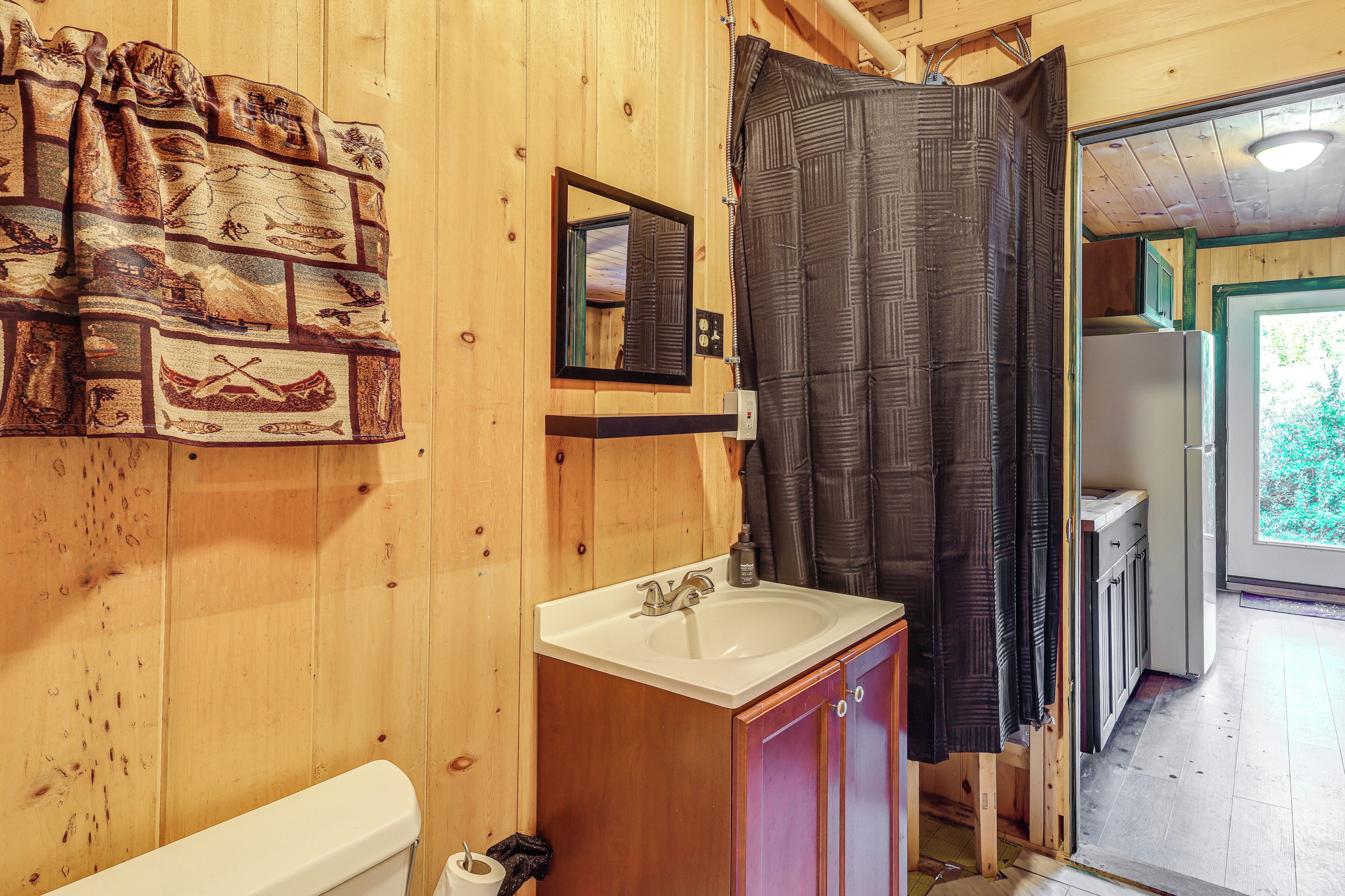 Une salle de bain rustique, aménagée dans une cabane en bois, avec un lavabo, un miroir et un rideau de douche.