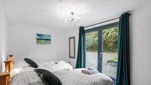 A bedroom with a bed, a radiator, a painting, and a view of a garden through a glass door. - Bracken Ground (Ulverston)
