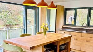 A modern kitchen with a wooden table, green chairs, and a vase of yellow flowers. - Bracken Ground (Ulverston)