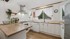 A modern kitchen with white cabinetry, a wooden countertop, a stainless steel refrigerator, and a window with white curtains.