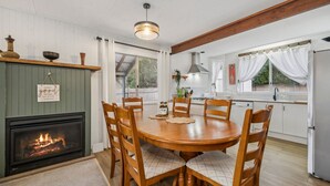 A cozy dining area with a wooden table and chairs, a fireplace, and a kitchen in the background.