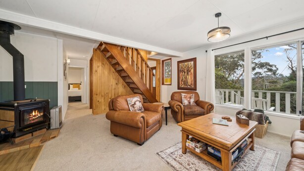 A cozy living room with a fireplace, leather sofas, a wooden coffee table, and a staircase leading to another room.