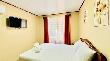 Une chambre d’hôtel avec un lit, un téléviseur à écran plat fixé au mur et une fenêtre avec des rideaux rouges.