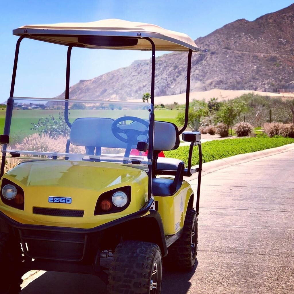 A yellow golf cart parked on a paved path with a mountainous landscape in the background.