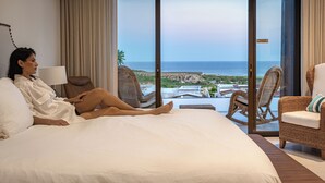 Una habitación de hotel con una cama grande, un sillón de mimbre y vistas al océano.