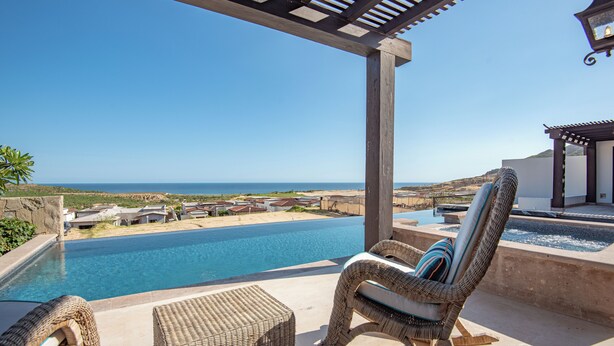 Zona de piscina con sillas de mimbre y vista al océano.