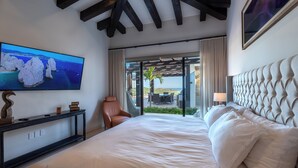 Habitación de hotel con una cama grande, un televisor en la pared, un sillón de cuero y vistas al exterior a través de amplias ventanas.