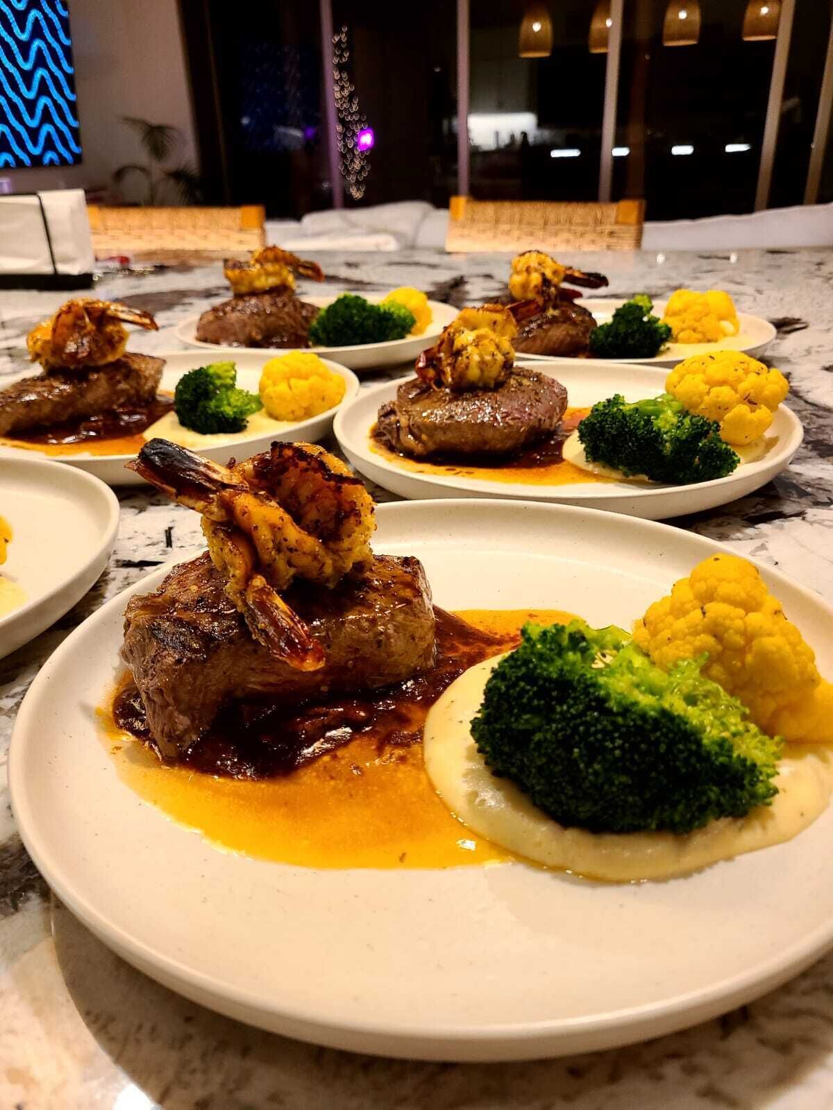 Una mesa de comedor con platos de comida, incluyendo carne, brócoli y coliflor.