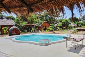 A swimming pool surrounded by thatched-roof structures and outdoor seating. - Wassado cultural lodging (Cap Skirring)