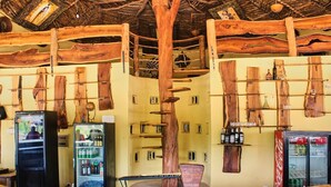 A rustic bar area with wooden furniture, a refrigerator, and shelves with bottles. - Wassado cultural lodging (Cap Skirring)