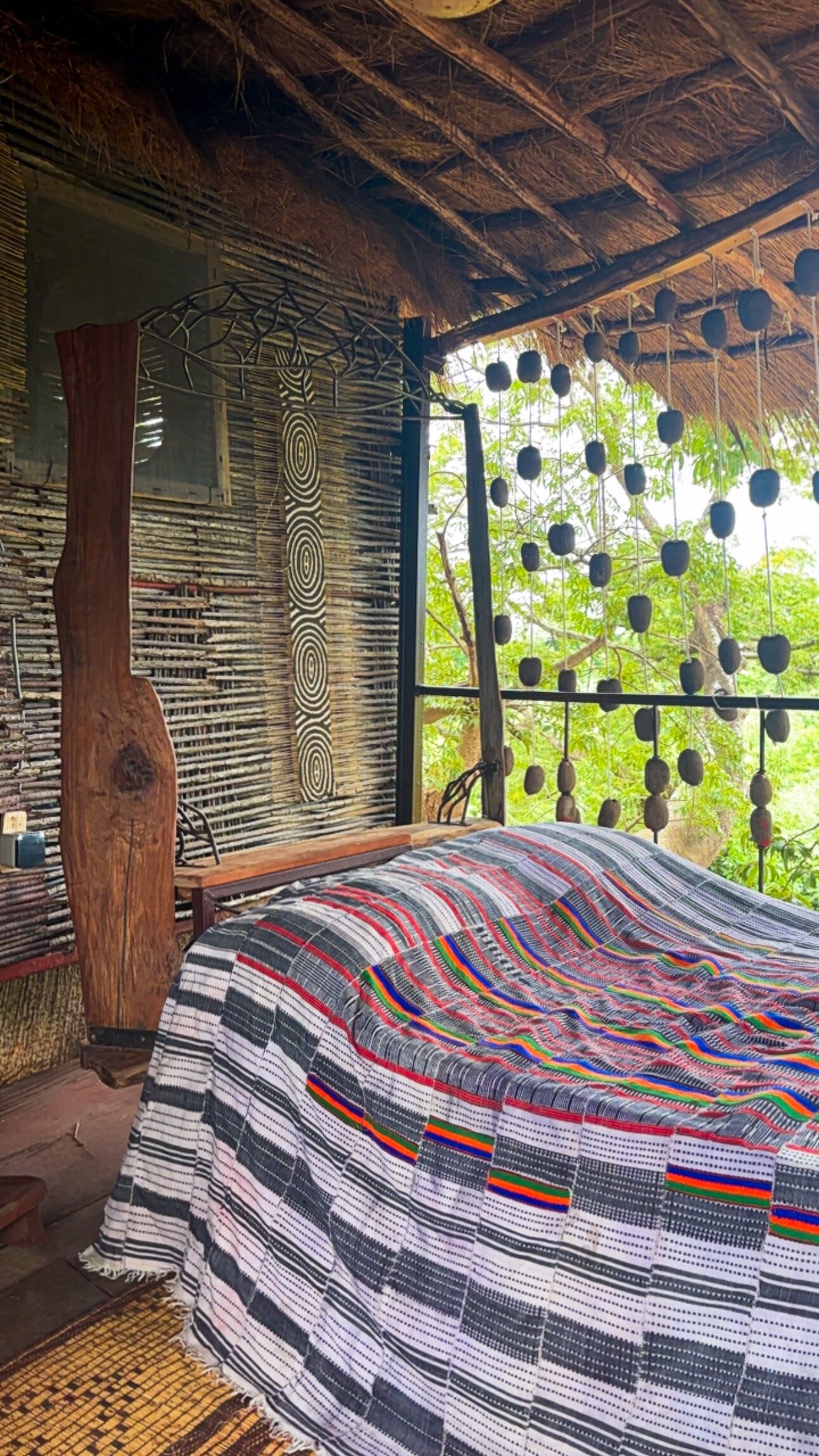 A room with a bed, a woven wall, and a view of trees.