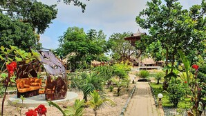 A garden pathway leading to a rustic-style building with a thatched roof, surrounded by lush greenery and a swing chair. - Wassado cultural lodging (Cap Skirring)