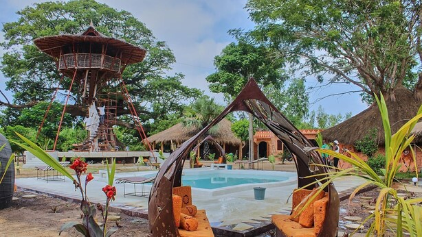 A pool area with a thatched-roof structure, a hanging chair, and a wooden tower. - Wassado cultural lodging (Cap Skirring)