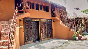 A traditional building with a thatched roof, a staircase with a red railing, and two large wooden doors with intricate carvings.