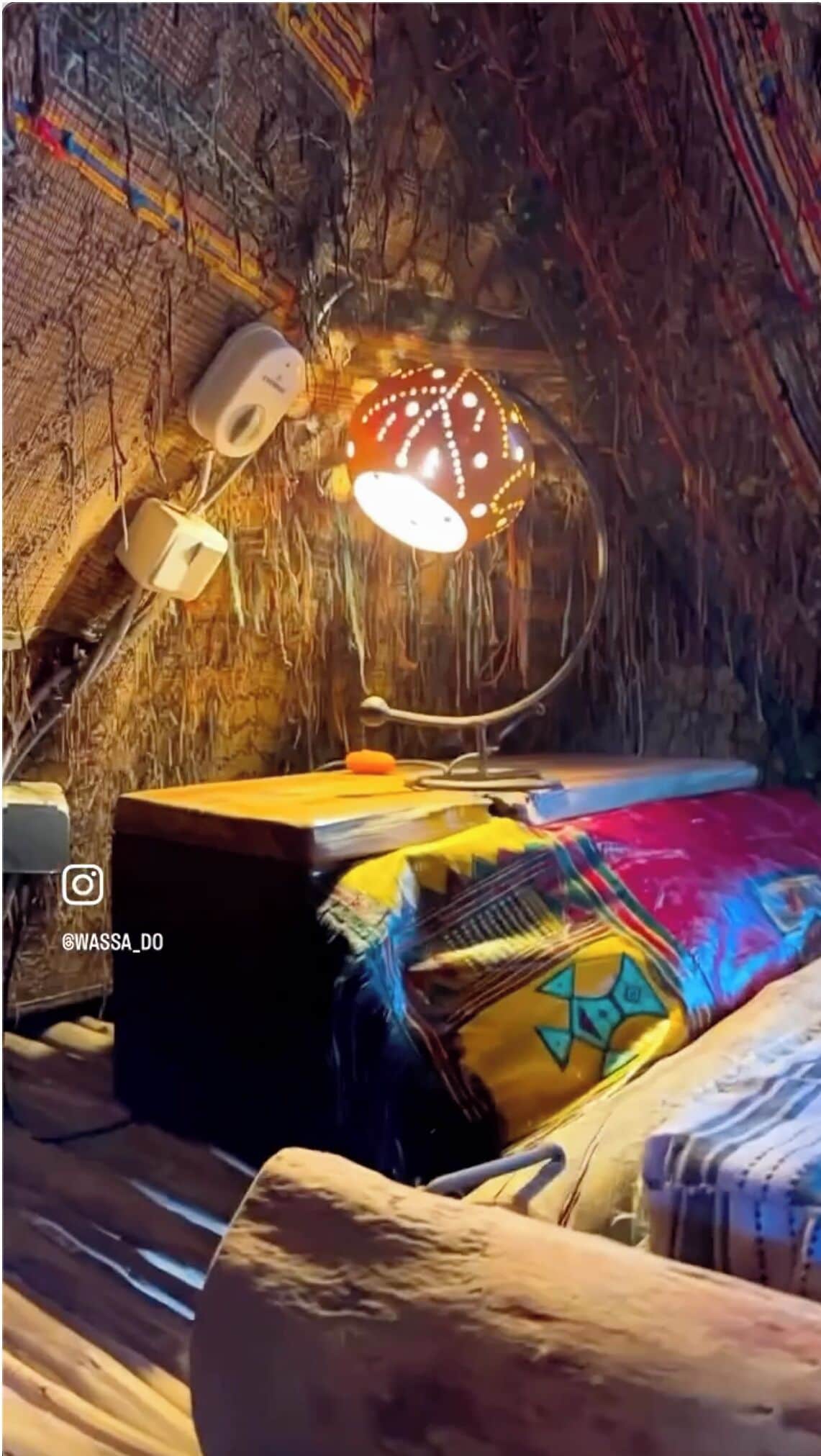 A cozy attic bedroom with a rustic aesthetic, featuring a unique lamp, a small table, and colorful bedding.