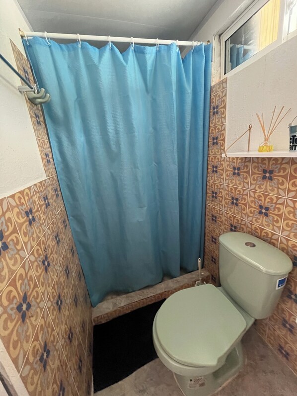 A bathroom with a toilet, a blue shower curtain, and patterned tiles. - Beach front bungalow with AC in Providencia (Providencia)