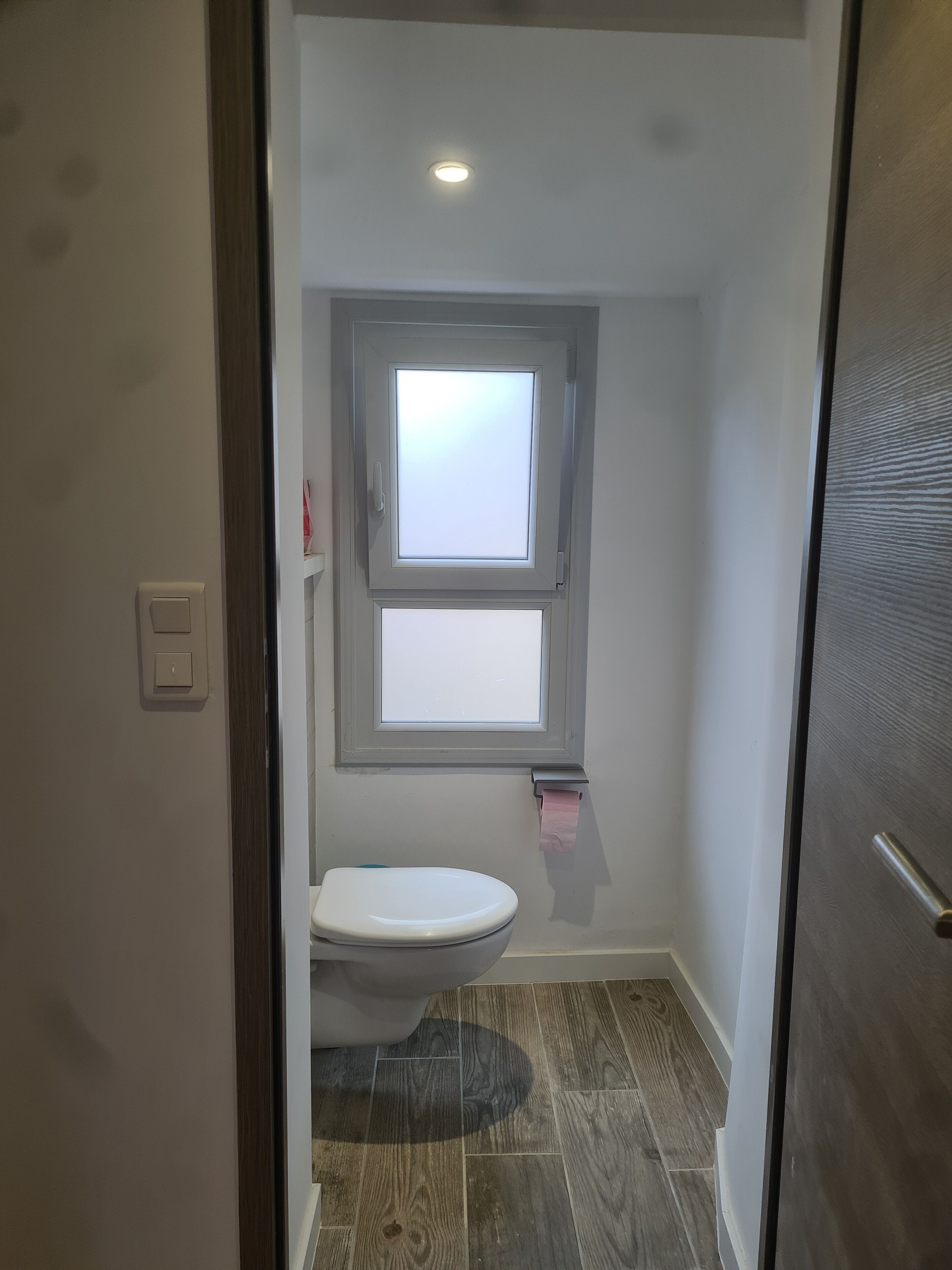 Une petite salle de bain avec des toilettes, une fenêtre et un plancher en bois.