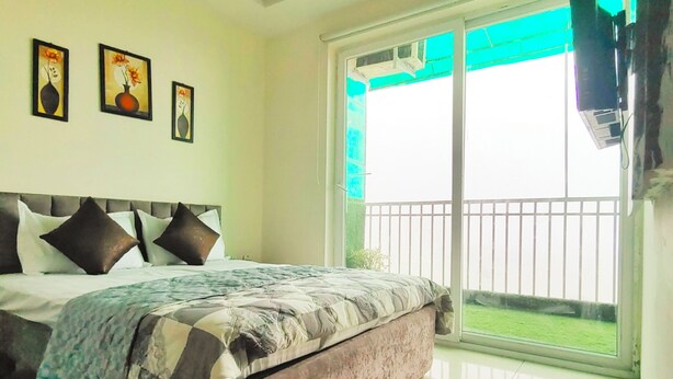 A bedroom with a bed, a ceiling fan, and a large window with a view of a balcony. - Charming Apartment with best Balcony & view in Zirakpur (Zirakpur)