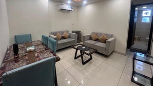 A living room with two sofas, a coffee table, a dining table with chairs, and an air conditioning unit on the ceiling. - Charming Apartment with best Balcony & view in Zirakpur (Zirakpur)