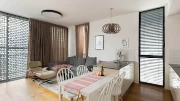 A modern living room with a dining area, featuring a sofa, chairs, a table with a placemat, and a kitchen area with a countertop and sink.