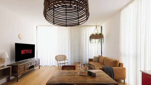 A modern living room with a wooden dining table, a sofa, a TV displaying 'NETFLIX', and a hanging plant. - Stylish Beach Getaway  Steps from Carmel Market! (Tel Aviv-Yafo)