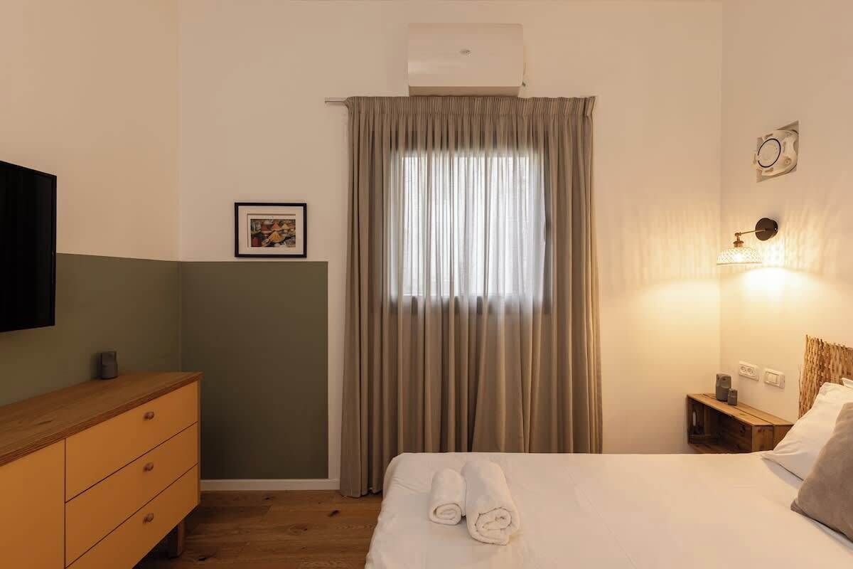 Een hotelkamer met een bed, een houten dressoir, een wandtelevisie, een raam met gordijnen en een bedlampje.