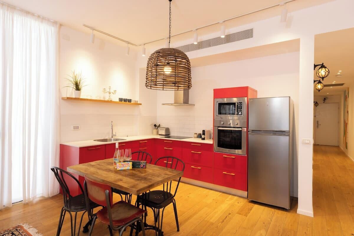Une cuisine moderne avec des meubles de couleur rouge, une table à manger en bois et des appareils électroménagers en acier inoxydable.