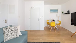 A modern living room with a sofa, a dining area with a table and chairs, and a door leading to another room.