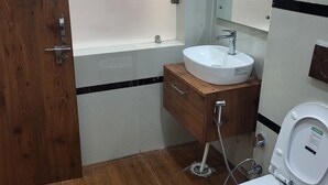 A bathroom with a wooden door, a white sink, a mirror, and a toilet. - Hotel MG Kitchen and Banquet (Kathua)