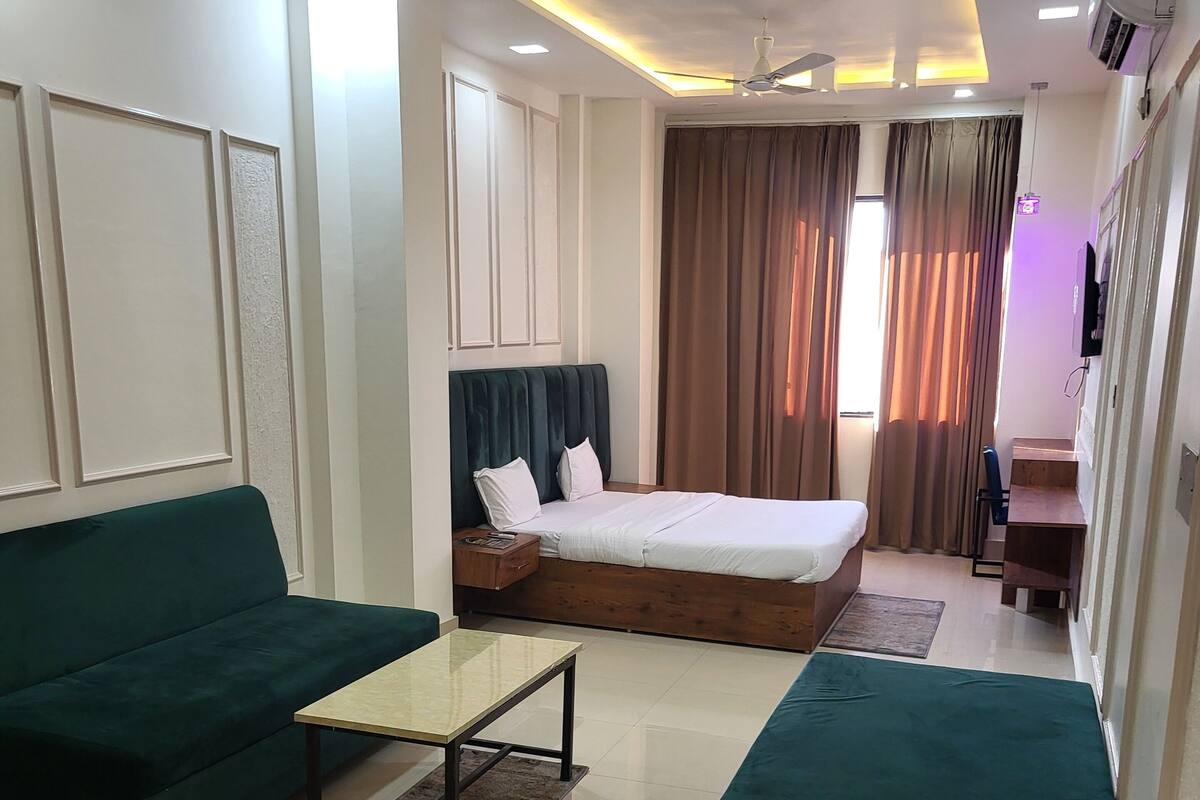 Una habitación de hotel moderna con una cama, sofás verdes, una mesita y un ventilador de techo.