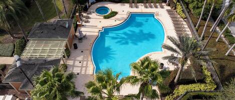 An aerial view of a swimming pool surrounded by palm trees, lounge chairs, and a small circular hot tub.
