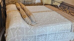 Habitació rústica amb parets de pedra, un llit, una cadira i una taula petita amb una làmpada.