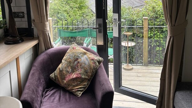 A room with a purple chair, a small table, and a view of a green garden through a sliding glass door.