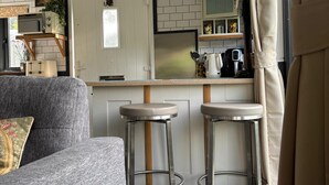 A compact living space with a sofa, two bar stools, a kitchenette, and a door with a decorative item.