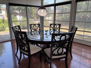 A dining area with a glass table and chairs, large windows, and a view of greenery and buildings.